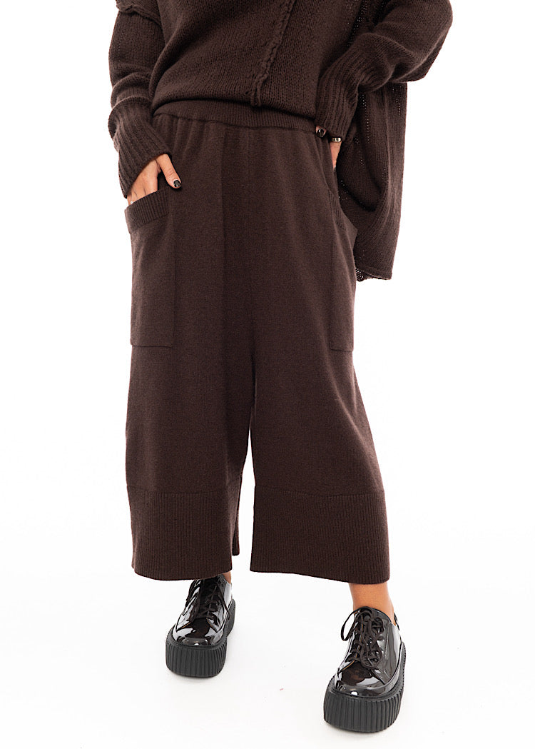 A Model wearing a Brown Knitted Skirt with pockets. Disclosing the big Pockets on the front of the piece.