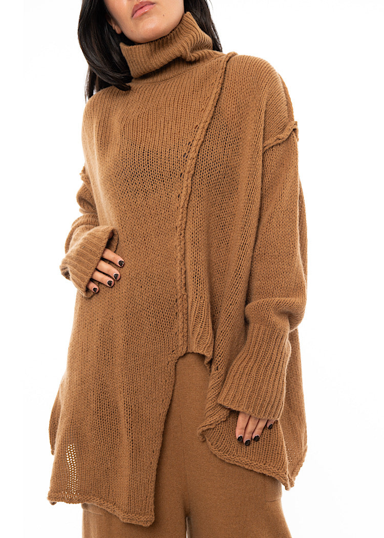 An up close oFf A Model wearing a light brown knitted Oversized Pullover with distressed pieces dangling down. Showing the distinct seam-lines.