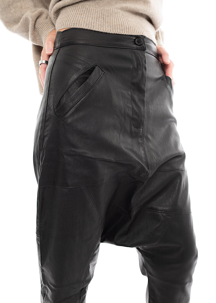 An up close of A Model wearing a Structured Drop-Crotch Black Leather Trouse. Showing the pockets and button to fasten.
