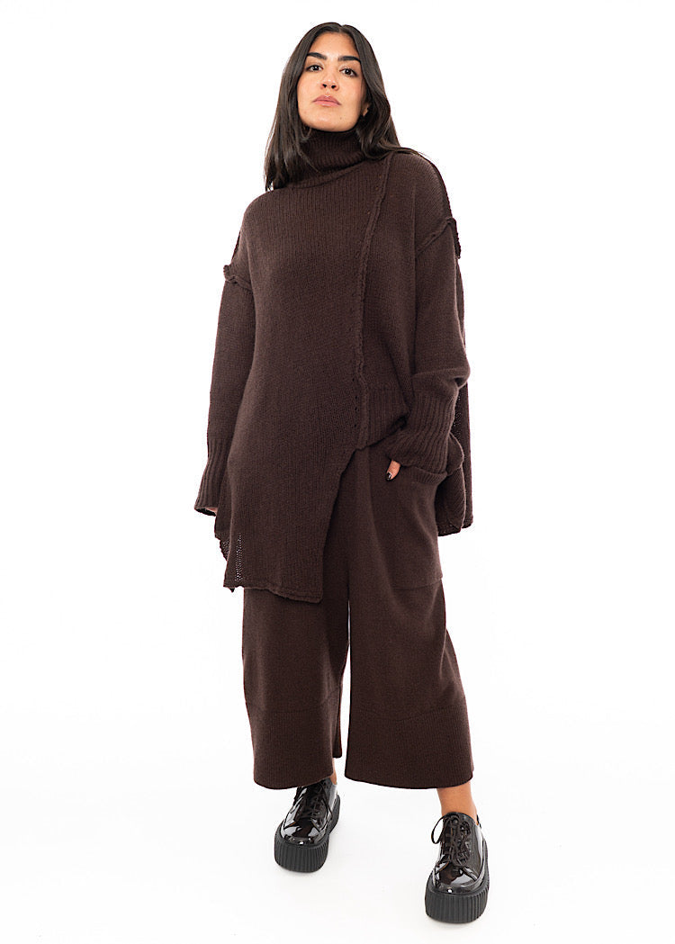 A full frame Photo of A Model wearing a Brown Knitted Skirt with pockets. Paired with a matching Pullover and Brown patent shoes.